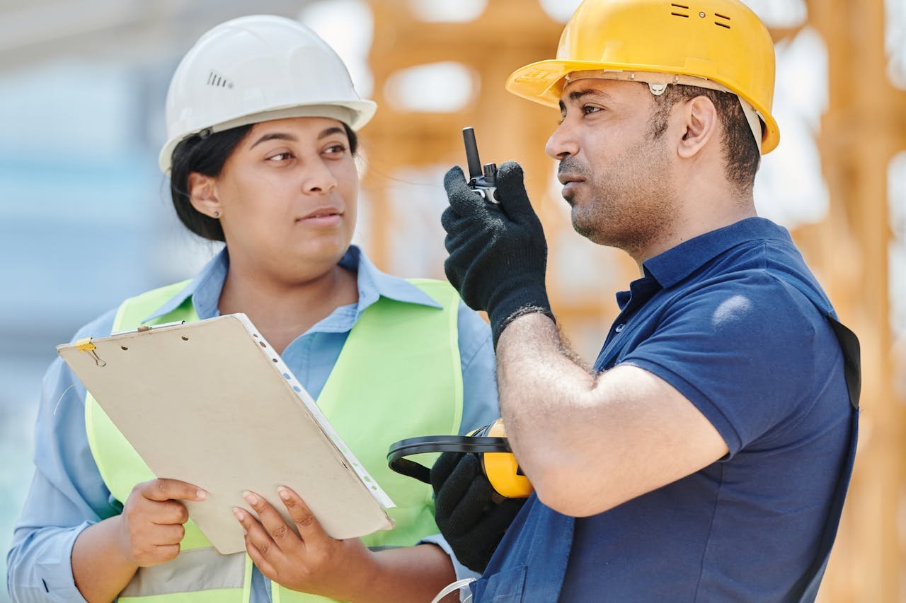 Two construction workers in safety gear discussing plans at a construction site.
